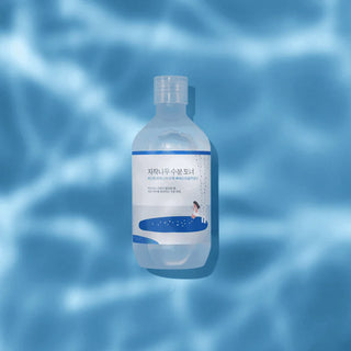 Round Lab Birch Juice Toner bouteille transparente sur fond bleu ondule evoquant l'eau et l'hydratation