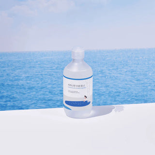 Round Lab Birch Juice Toner pose sur surface blanche avec ocean bleu en arriere-plan, ambiance fraicheur