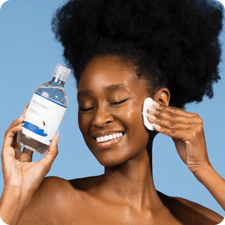 Femme souriante appliquant le Round Lab Birch Juice Toner avec un coton sur le visage, fond bleu