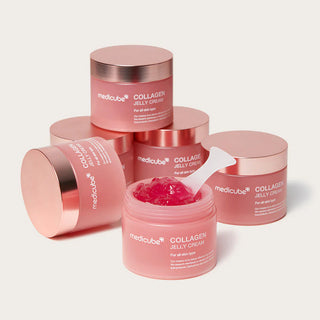 Cinq pots roses Medicube Collagen Jelly Cream empiles, pot ouvert au premier plan avec spatule dans la gelee rose vif