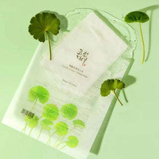 Sachet Beauty of Joseon Centella Calming Mask sur fond vert pastel avec feuilles de centella fraiches et gel transparent