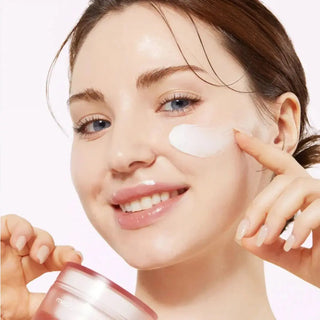 Gros plan d'une femme souriante appliquant la creme Medicube Triple Collagen sur sa joue