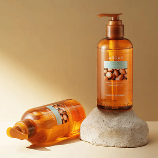 Nature Republic Argan Shampoo - deux flacons pompe ambres poses sur une pierre beige, fond dore
