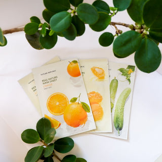 Quatre sachets Nature Republic Real Nature poses en eventail avec branche de plante verte, variantes orange et concombre