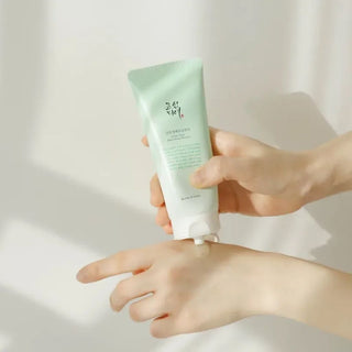 Mains pressant le tube Beauty of Joseon Green Plum Cleanser sur le dos de la main, lumiere naturelle