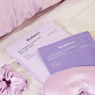 Boite et sachet BIODANCE Caviar PDRN poses sur draps satin rose avec chouchou et masque de nuit assortis