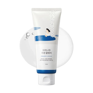Tube ROUND LAB Birch Juice Moisturizing Cleanser 150ml devant un swatch de texture nettoyante blanche et bulles