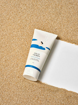 Tube ROUND LAB Birch Juice Moisturizing Cleanser 150ml posé sur du sable, à côté d'une bande de papier blanc
