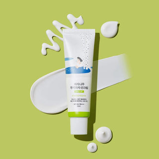 Round Lab Birch Mild-Up Sunscreen SPF50+ sur fond vert avec eclats de creme blanche autour du tube