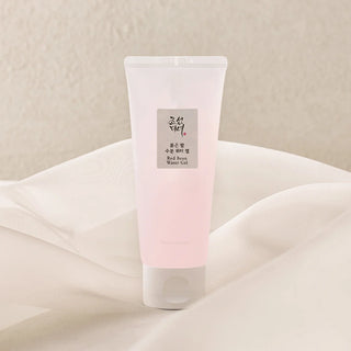 Tube Beauty of Joseon Red Bean Water Gel pose sur tissu soyeux blanc, fond beige chaleureux