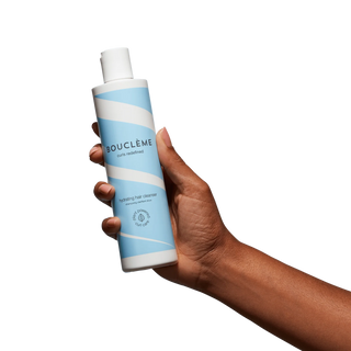 Main tenant le flacon Boucleme Hydrating Hair Cleanser 300 ml bleu et blanc sur fond blanc