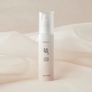 Flacon Beauty of Joseon Ginseng Moist Sun Serum sur fond beige avec drapé de tissu soyeux
