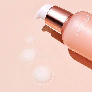 Gros plan flacon Medicube Triple Collagen Serum couche, gouttes de serum translucide sur fond rose