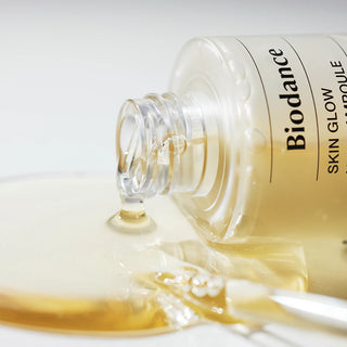 Flacon BIODANCE Skin Glow Vital Ampoule couche sur le cote, serum dore qui coule sur surface blanche