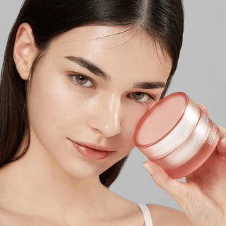 Jeune femme tenant le pot rose Medicube Triple Collagen Cream pres de son visage sur fond gris