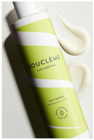 Flacon vert Boucleme Curl Cleanser penche avec touche de creme blanche sur fond clair