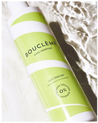 Flacon vert Boucleme Curl Cleanser pose pres de l'eau, etiquette creme lavante non moussante visible