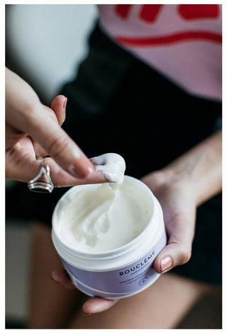 Boucleme Intensive Moisture Treatment - mains prelevant la creme blanche dans le pot ouvert, texture onctueuse