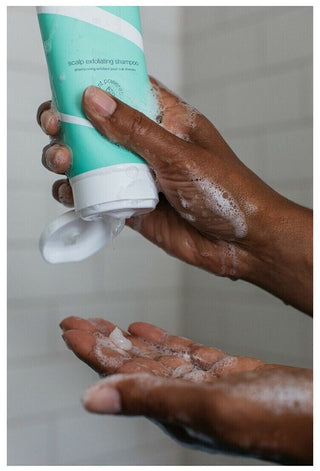 Mains pressant le tube vert Boucleme Scalp Exfoliating Shampoo avec mousse dans la paume