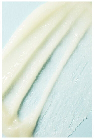 Texture cremeuse jaune pale etalee en traits sur fond bleu clair, shampooing exfoliant Boucleme