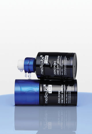 Deux flacons Medicube Zero Pore One Day Serum poses sur surface bleue avec gouttes de serum au compte-gouttes