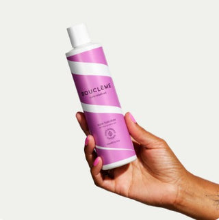 Main tenant le flacon rose et blanc Boucleme Super Hold Styler 300ml sur fond beige