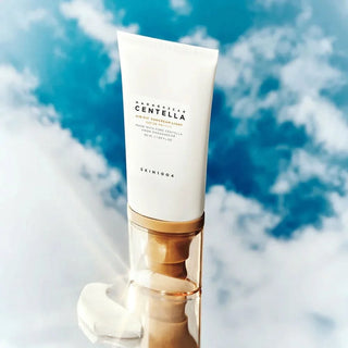 Tube SKIN1004 Centella Suncream Light SPF50+ pose sur un socle dore avec ciel bleu et nuages en fond