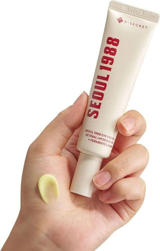 Main tenant le tube KSECRET Seoul 1988 Eye Cream avec noisette de creme jaune sur le pouce