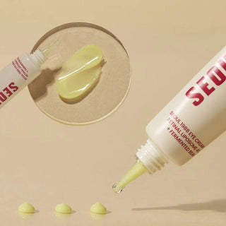 Texture jaune-vert du Seoul 1988 Eye Cream K-Secret deposee sur coupelle en verre et gouttes sur fond beige