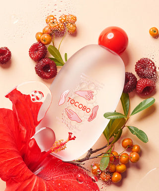 Flacon TOCOBO Vita Berry Pore Toner 150ml pose a plat entoure de framboises, baies et fleur d'hibiscus rouge
