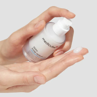 Main tenant le flacon pompe Medicube Zero Pore Serum 2.0 avec une goutte de serum transparent sur la paume