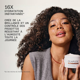 Femme aux cheveux boucles tenant le pot Olaplex Rich Hydration Mask avec texte 16x hydratation instantanee