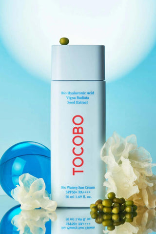 TOCOBO Bio Watery Sun Cream avec haricots mungo et fleurs blanches sur fond bleu