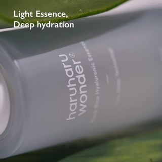 Gros plan du flacon Haruharu Wonder Black Rice Essence pose sur des feuilles vertes tropicales