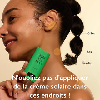 Femme souriante appliquant le stick Haruharu Wonder Black Bamboo Sun Shield sur les zones oubliées - oreilles, cou, épaules