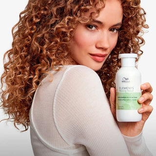 Wella Elements Renewing Shampoo - mannequin aux boucles cuivrees tenant le flacon