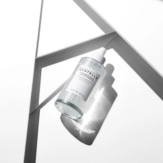 Flacon SKIN1004 Centella Ampoule en équilibre sur une structure géométrique grise avec reflet de lumière