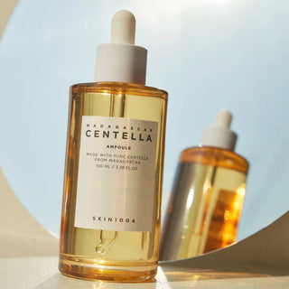 Trois flacons SKIN1004 Centella Ampoule disposes sur surface blanche avec ombres portees et lumiere naturelle