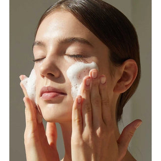 Femme aux yeux fermes massant une mousse nettoyante blanche sur ses joues