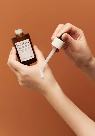 Mains déposant une goutte de texture lactée SKIN1004 Probio-Cica avec la pipette sur le dos de la main