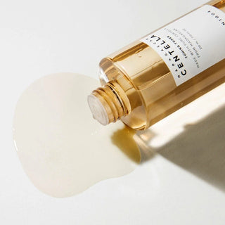 Flacon SKIN1004 Centella Toning Toner couche sur le cote avec toner dore qui coule sur surface blanche