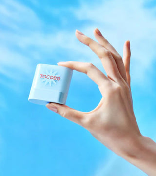 Main tenant le mini stick solaire TOCOBO entre deux doigts devant un ciel bleu ensoleillé